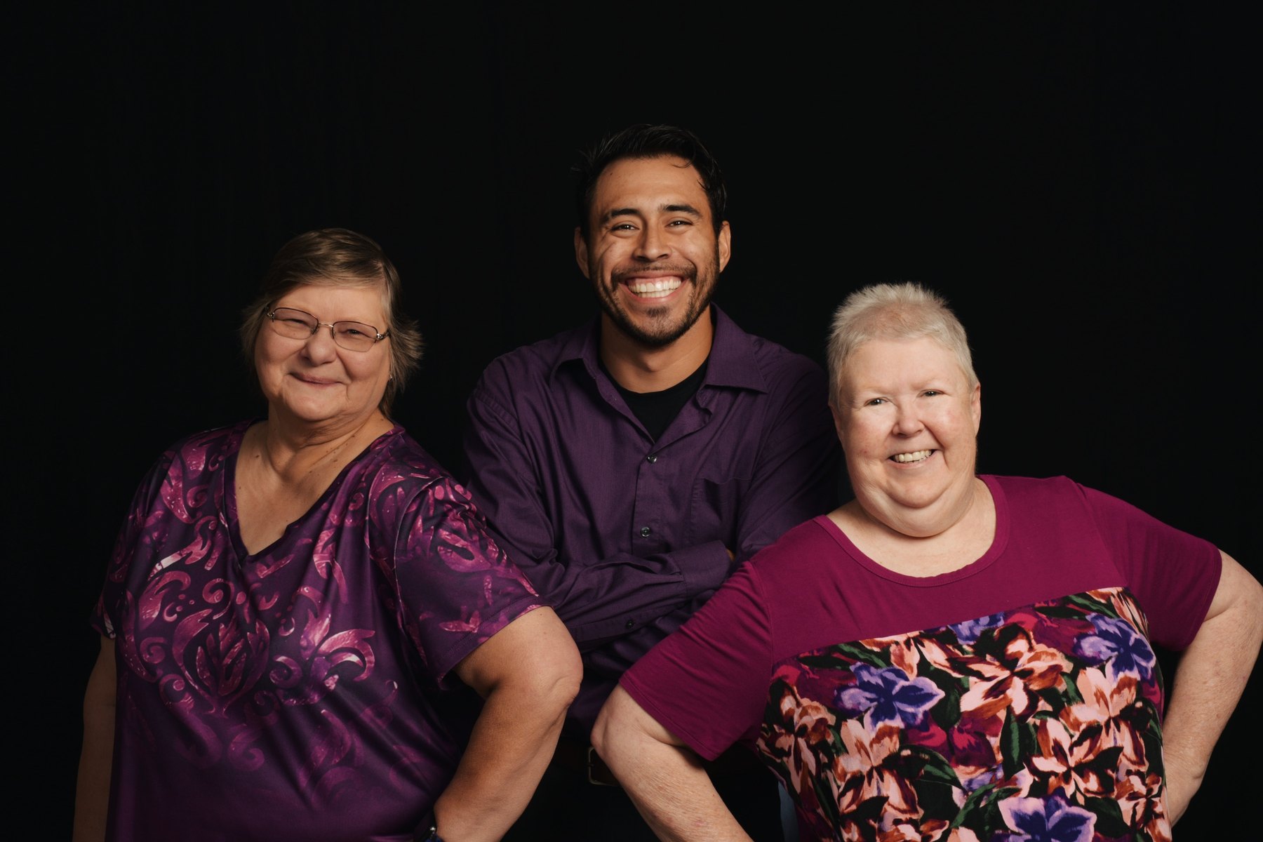 Lorenzo Marez seated between two women he photographed, all three laughing, against a black studio backdrop