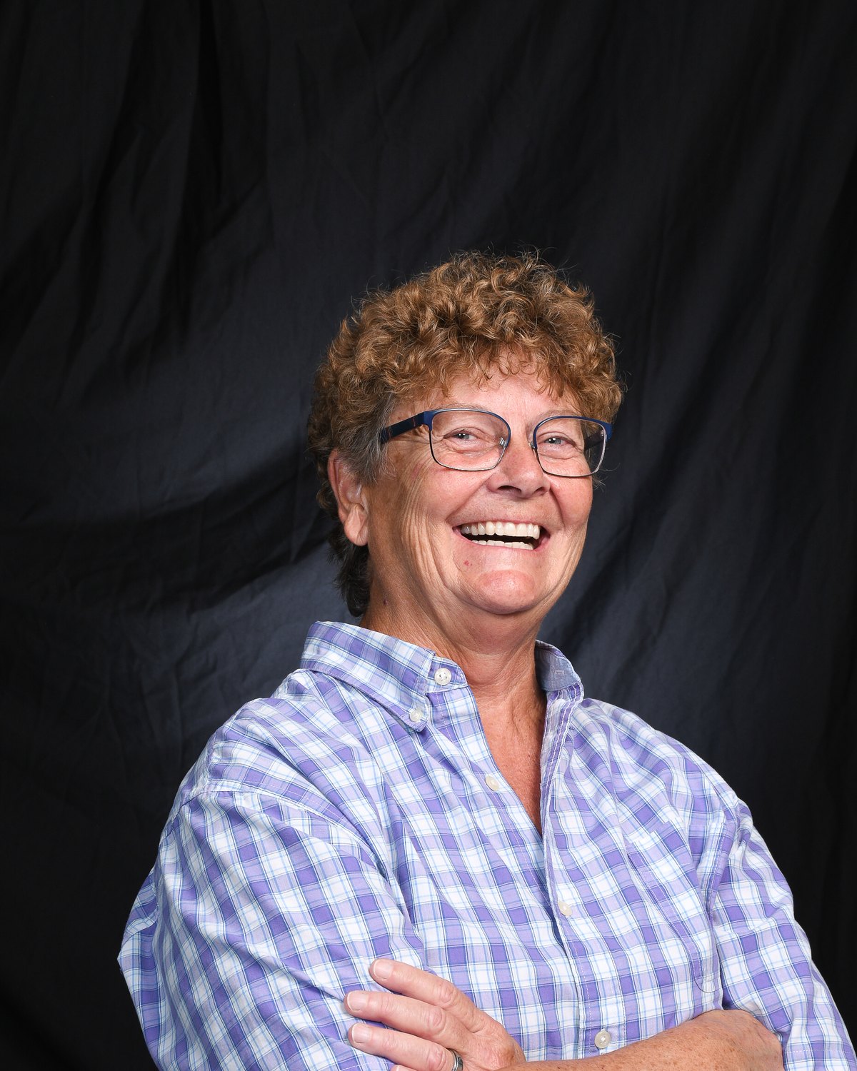 Portrait of a woman laughing with her arms folded, against a black backdrop